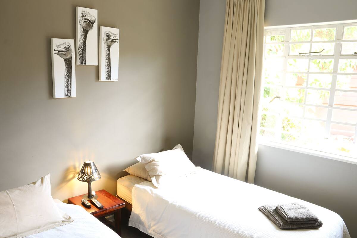 A hotel room with two beds, a nightstand with a lamp, and artwork on the wall.