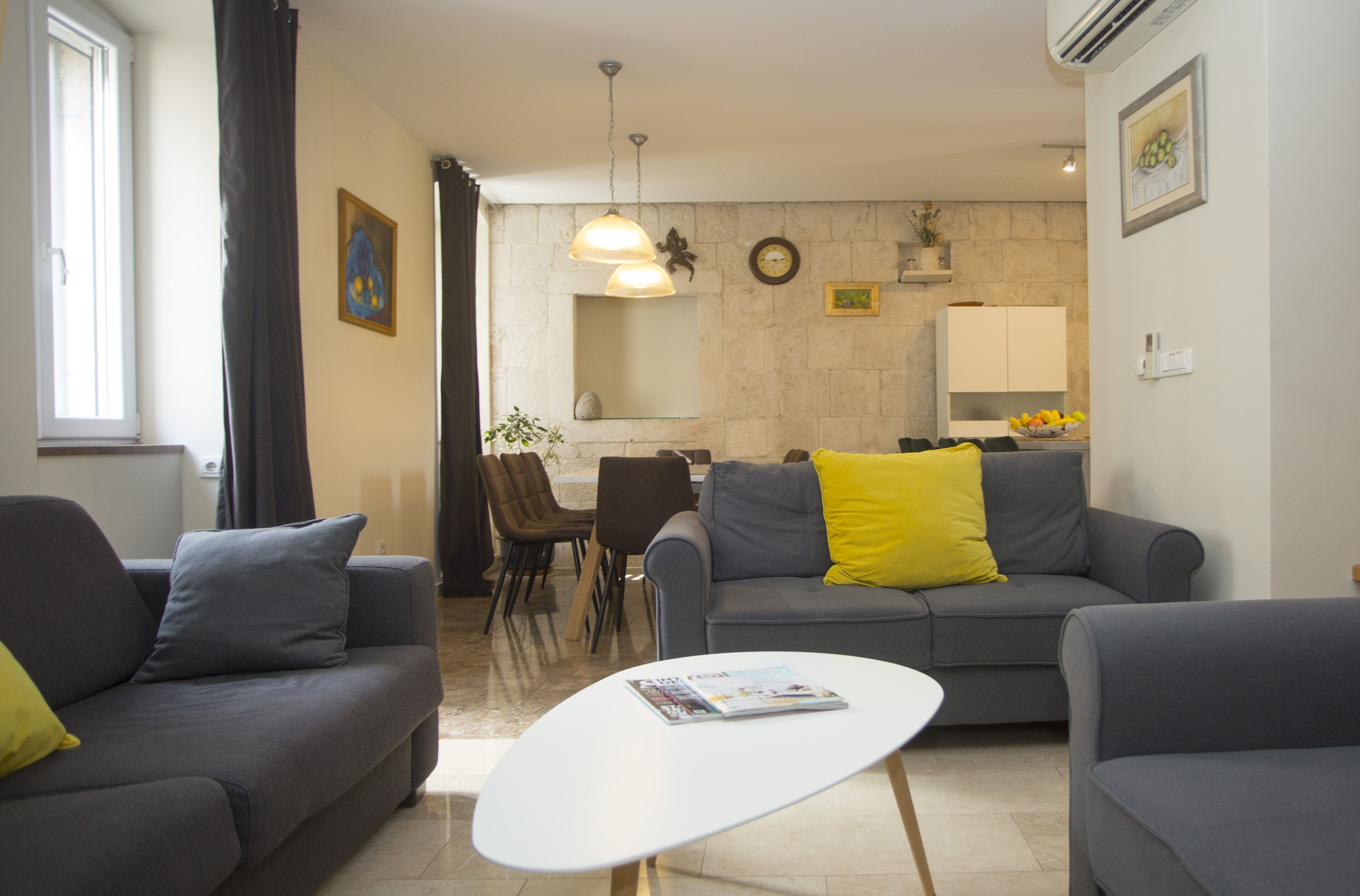 A modern living room with grey sofas, a white coffee table, and a dining area with chairs and a table.