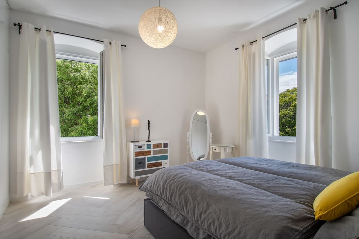 A bedroom with a bed, a dresser, a mirror, and a window with curtains.