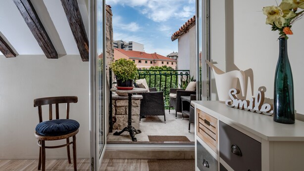 A balcony with a view of buildings, a wicker table with chairs, a potted plant, and a vase with flowers. - Bouganvillea Split Apartments (Split)