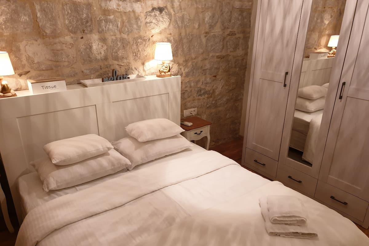 A neatly made bed with white linens and pillows, a bedside table with a lamp, and a wardrobe with a mirror.