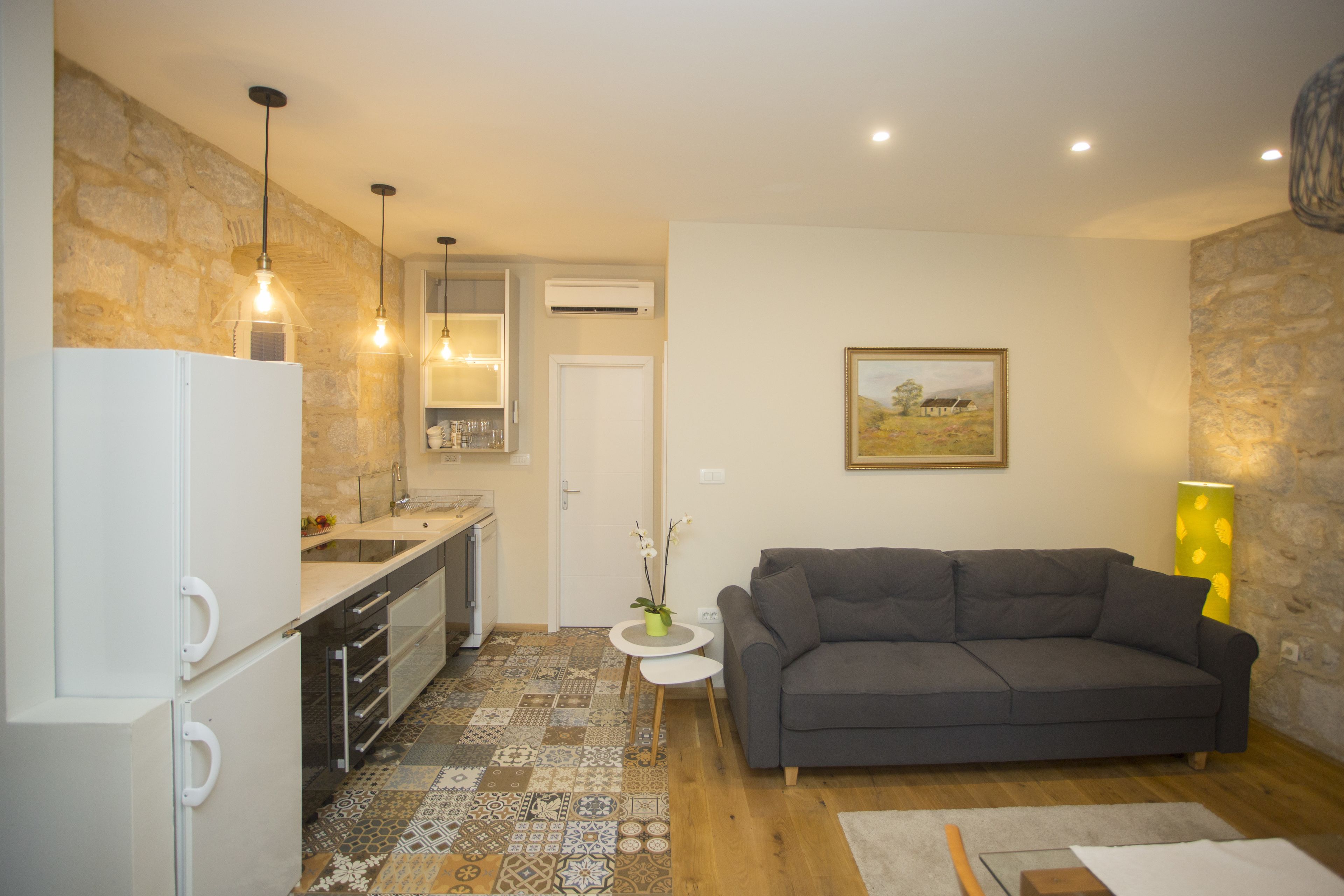 A compact living space with a kitchenette, a gray sofa, and a patterned floor.