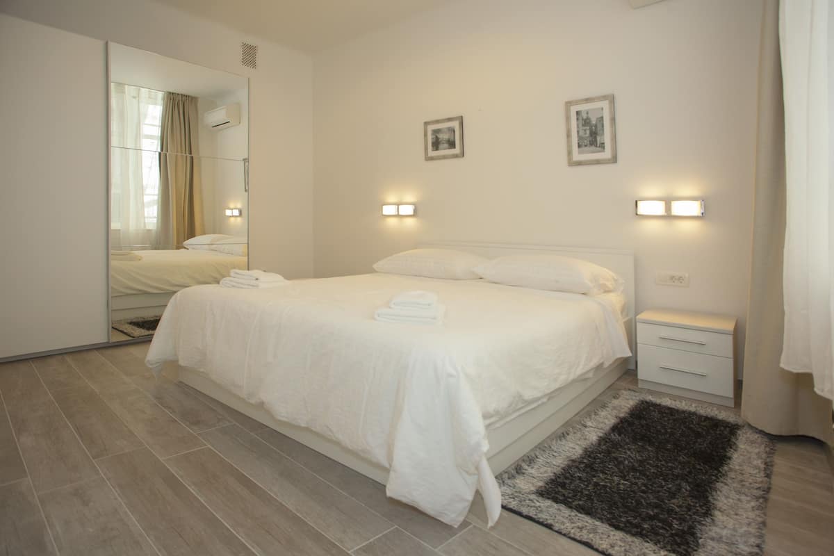 A modern hotel room with a large bed, a bedside table, and a mirror.