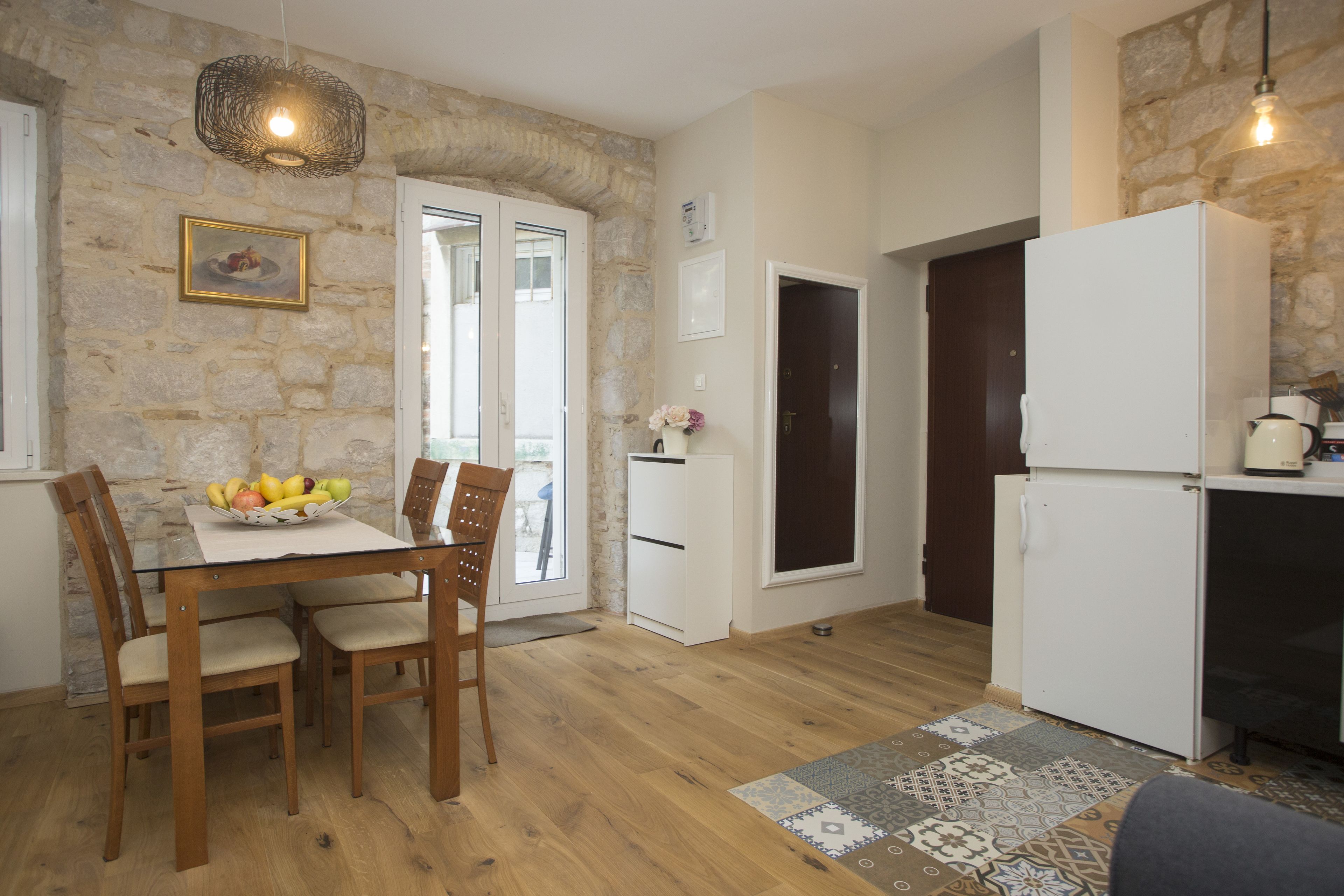 A kitchen with a dining table, chairs, a refrigerator, and a stone wall.