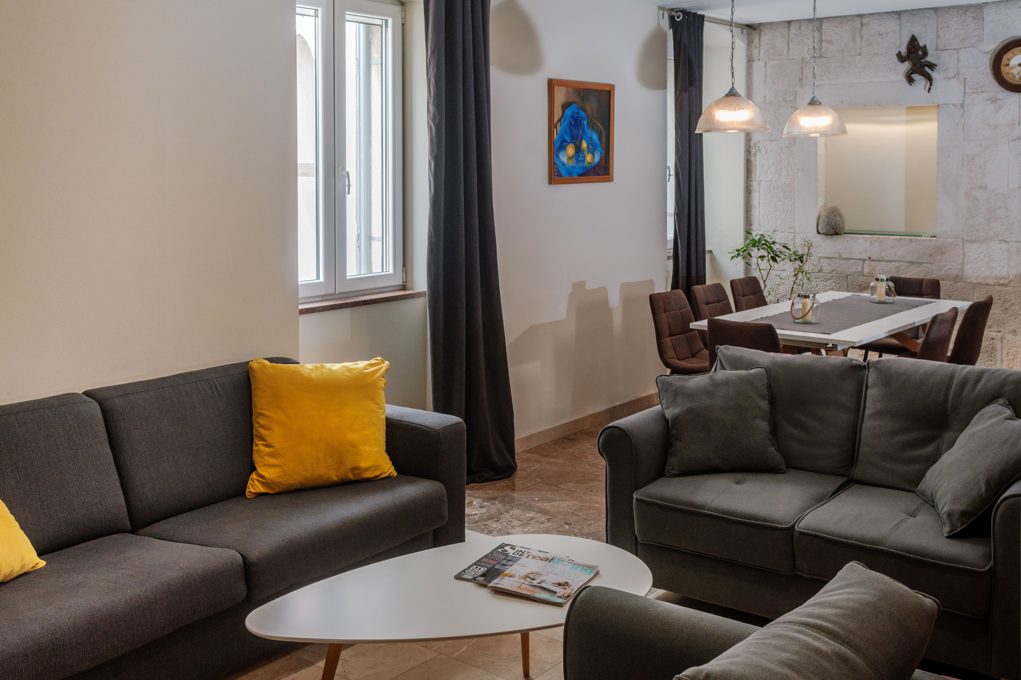 Un salon moderne avec un canapé gris, une table basse blanche et un coin repas comprenant une table et des chaises.