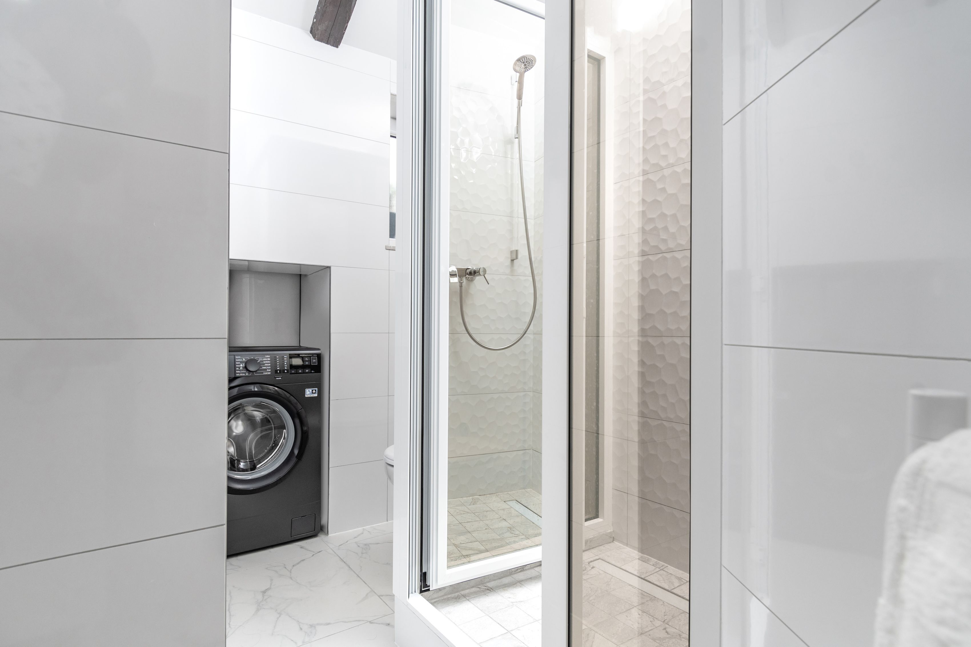 A modern bathroom with a glass-enclosed shower, a washing machine, and a tiled floor.