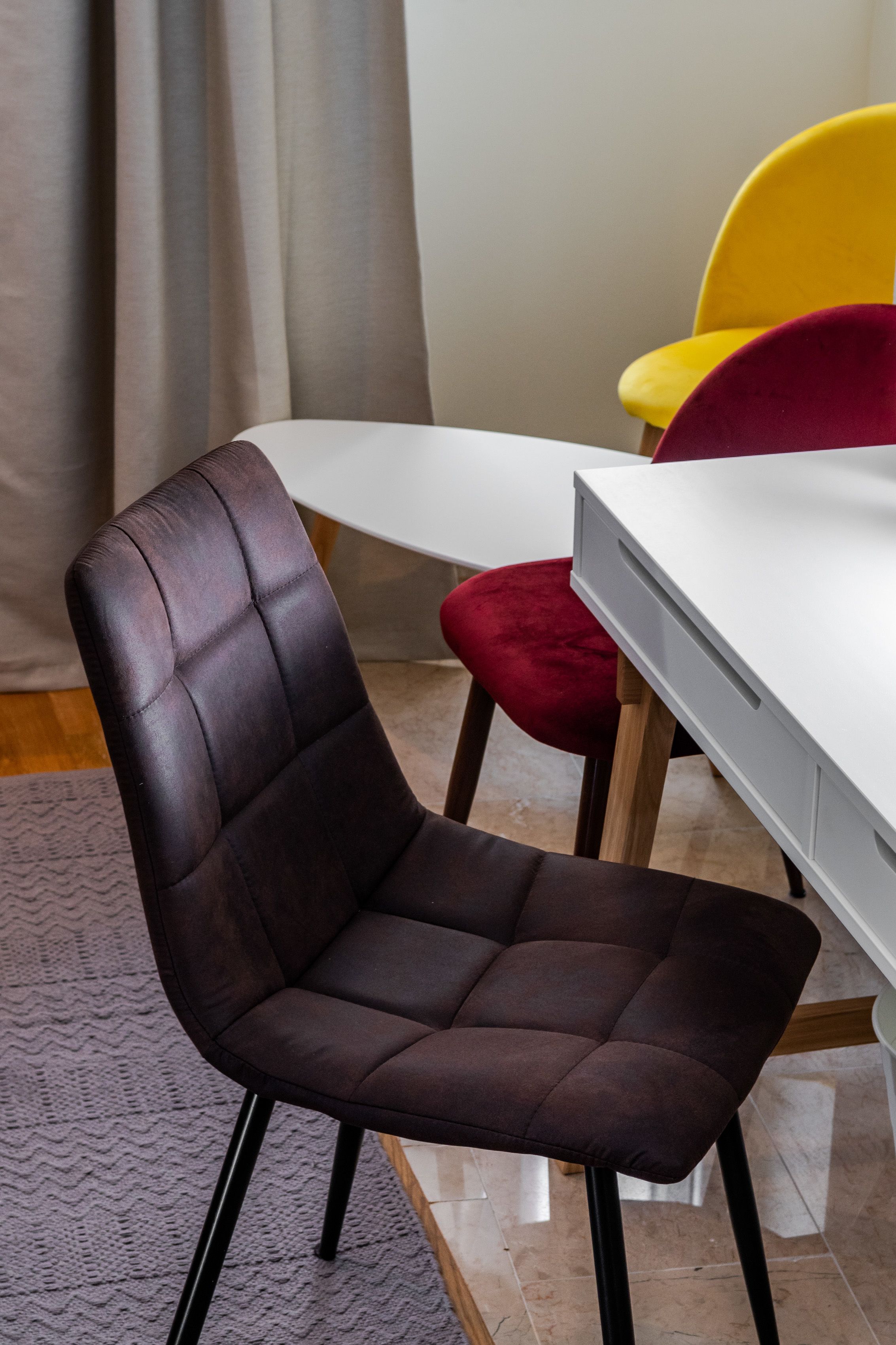Un comedor moderno con una silla tapizada marrón oscuro, un taburete con cojín rojo y una mesa blanca.