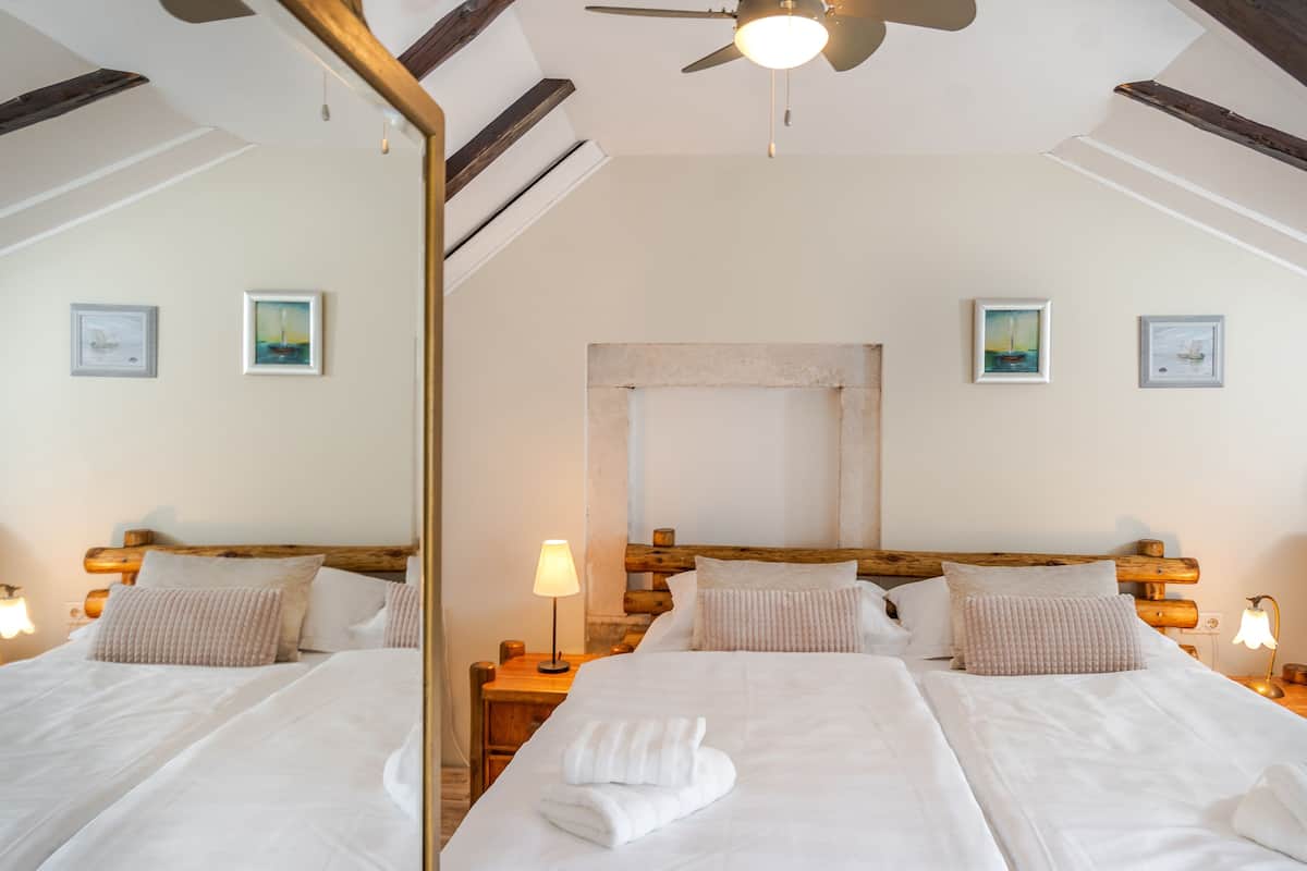 A hotel room with two beds, wooden headboards, a ceiling fan, and framed artwork on the walls.