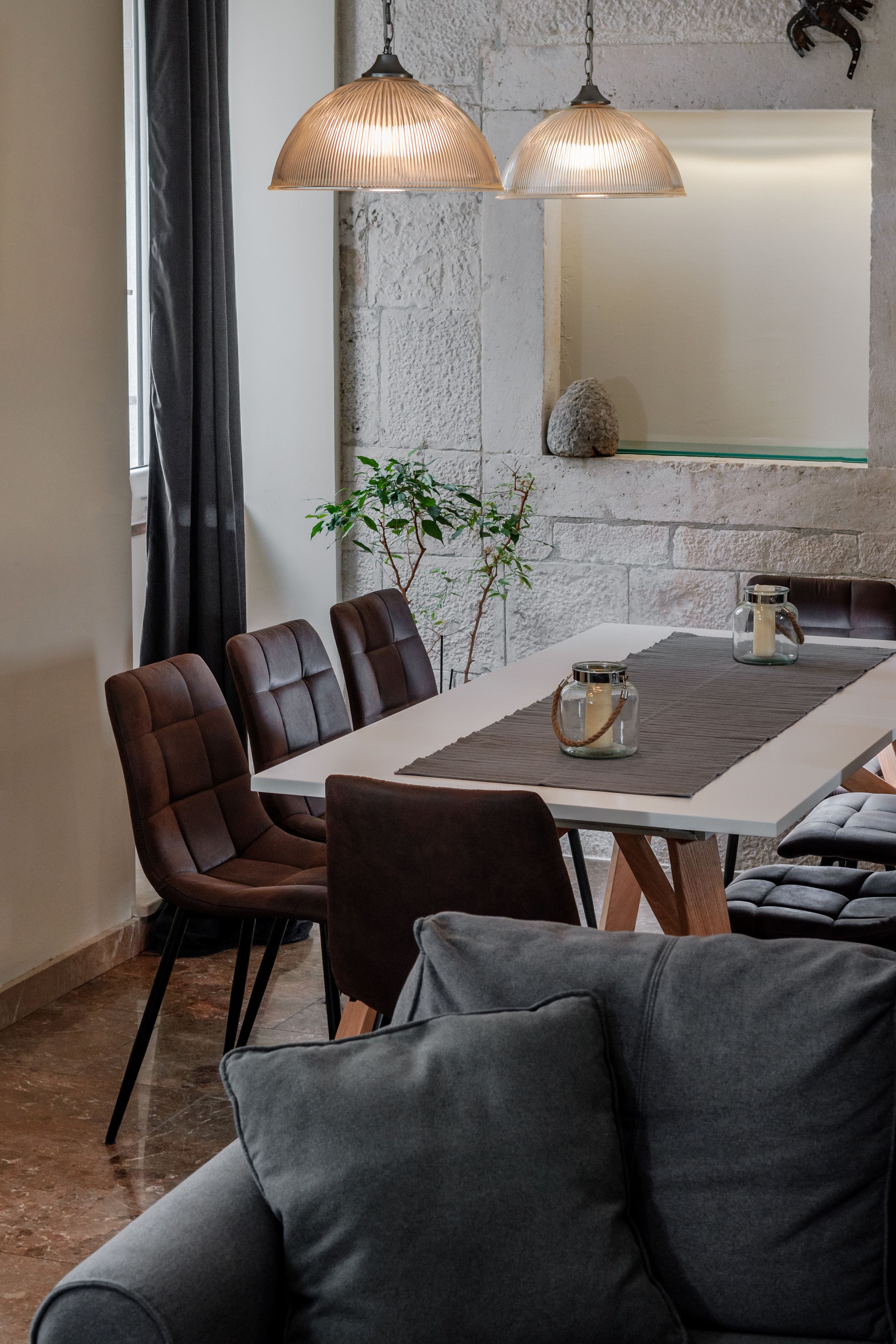 A modern dining area with a white table, brown upholstered chairs, and two pendant lights.