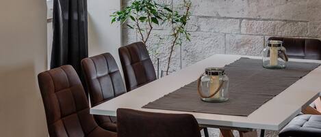 A modern dining area with a white table, brown upholstered chairs, and two pendant lights.