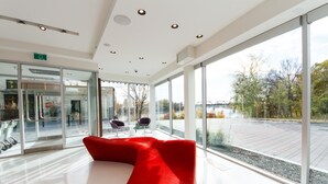 A modern interior with large windows, a red seating area, and a glass elevator. - Mere Hotel (Winnipeg)