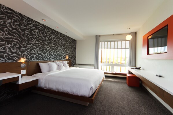 Una habitación de hotel moderna con una cama grande, una mesita de noche, un espejo y una ventana con cortinas.