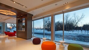 A modern interior with large windows, red and green seating, and a view of a snowy landscape. - Mere Hotel (Winnipeg)