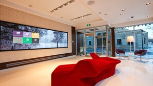 A modern lobby with a large digital display, red seating, and a glass entrance. - Mere Hotel (Winnipeg)