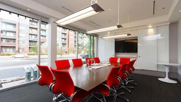A conference room with a long table, red chairs, and large windows offering a view of buildings and a street.