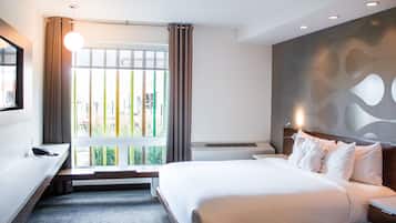 A hotel room with a bed, bedside table, and a large window with curtains.