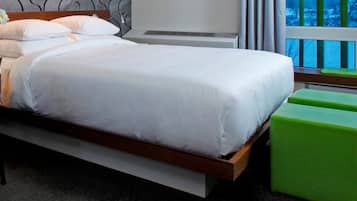 Un lit bien fait, avec du linge de lit blanc, une table de chevet avec une lampe et une fenêtre donnant sur des arbres.