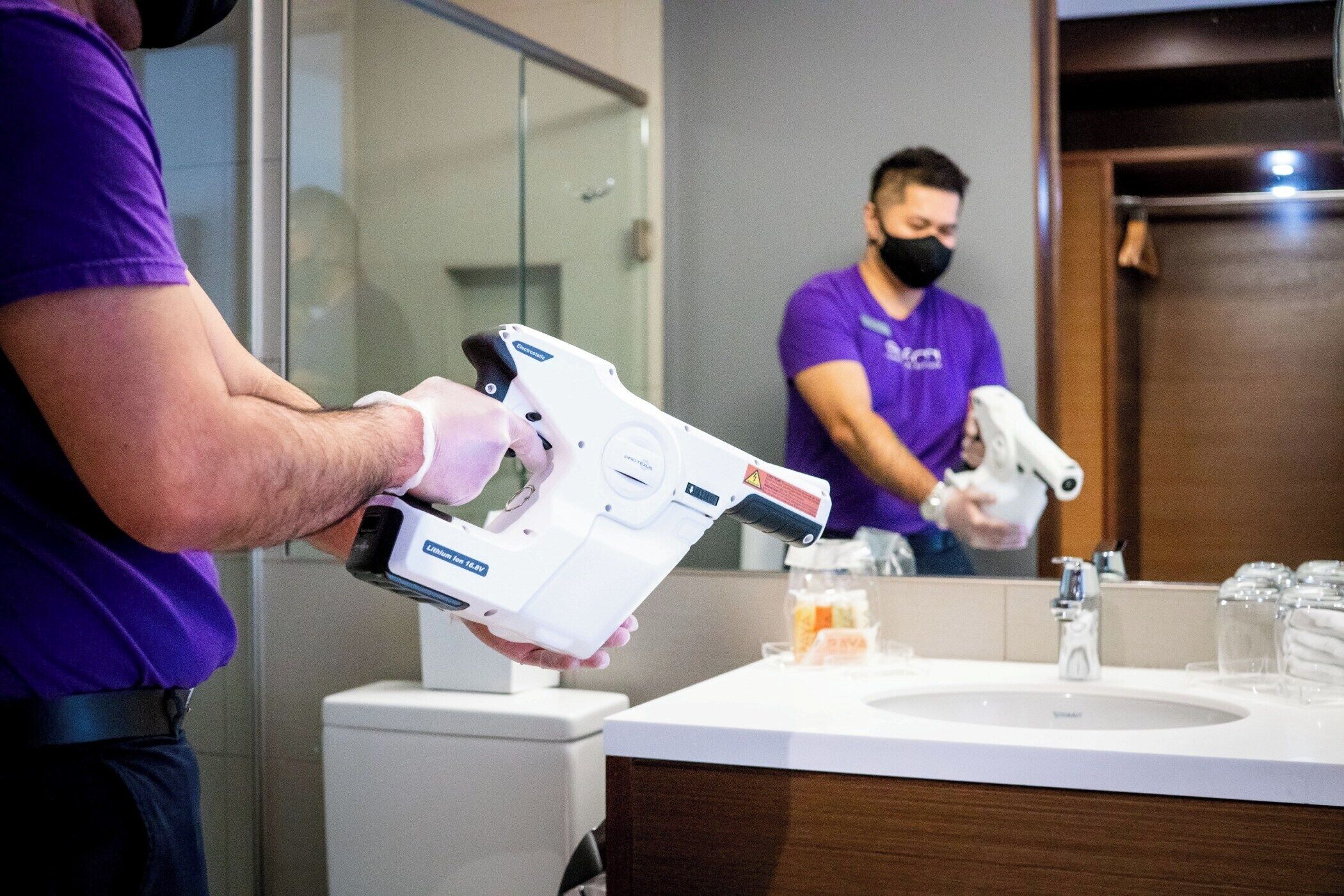 A person holding a white device in a bathroom with a sink, mirror, and toiletries.