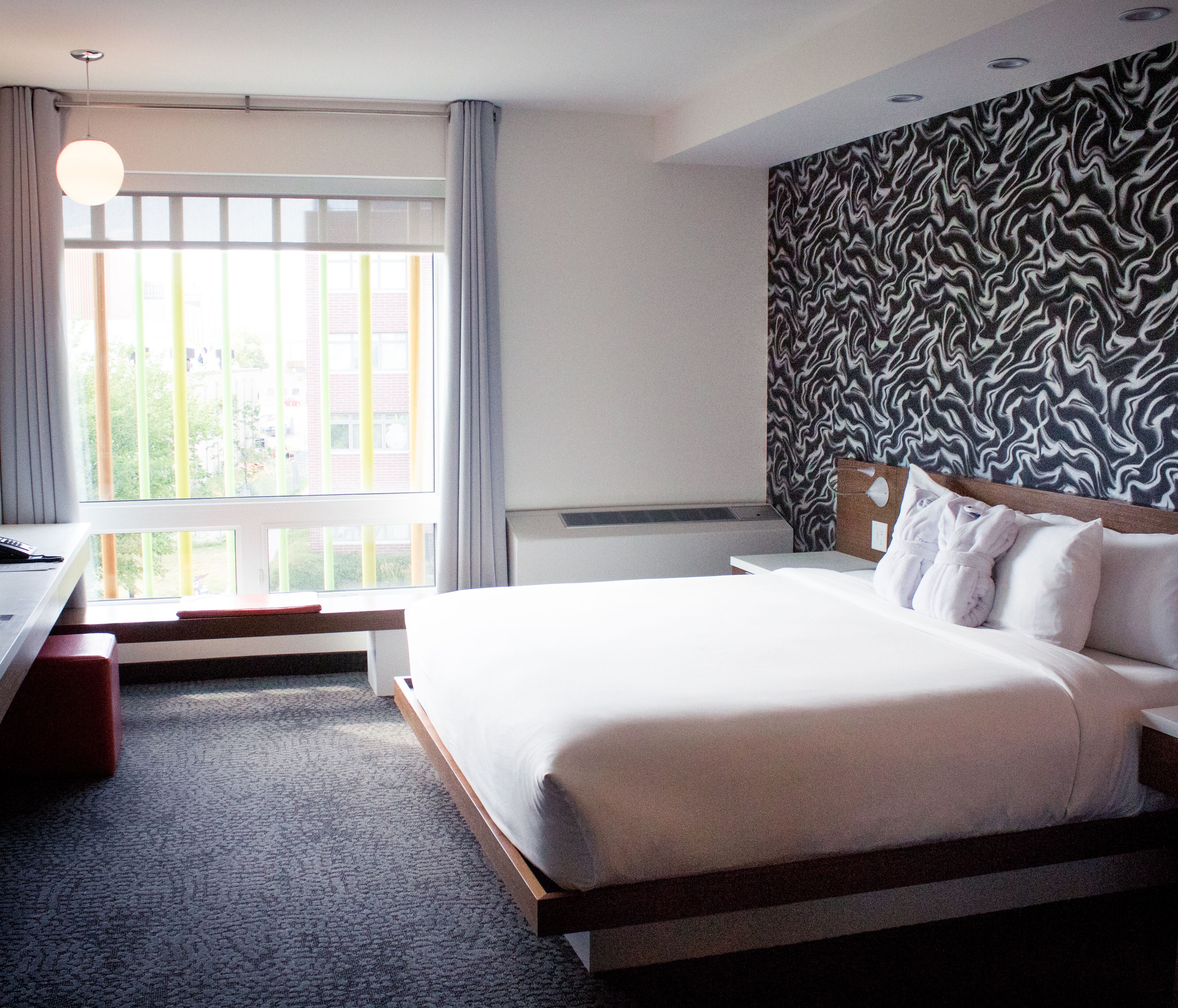 Habitación de hotel con una cama grande, un escritorio, una silla, una ventana con cortinas y un papel tapiz estampado.