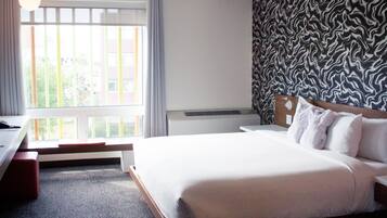 A hotel room with a large bed, a desk, a chair, a window with curtains, and a patterned wall.