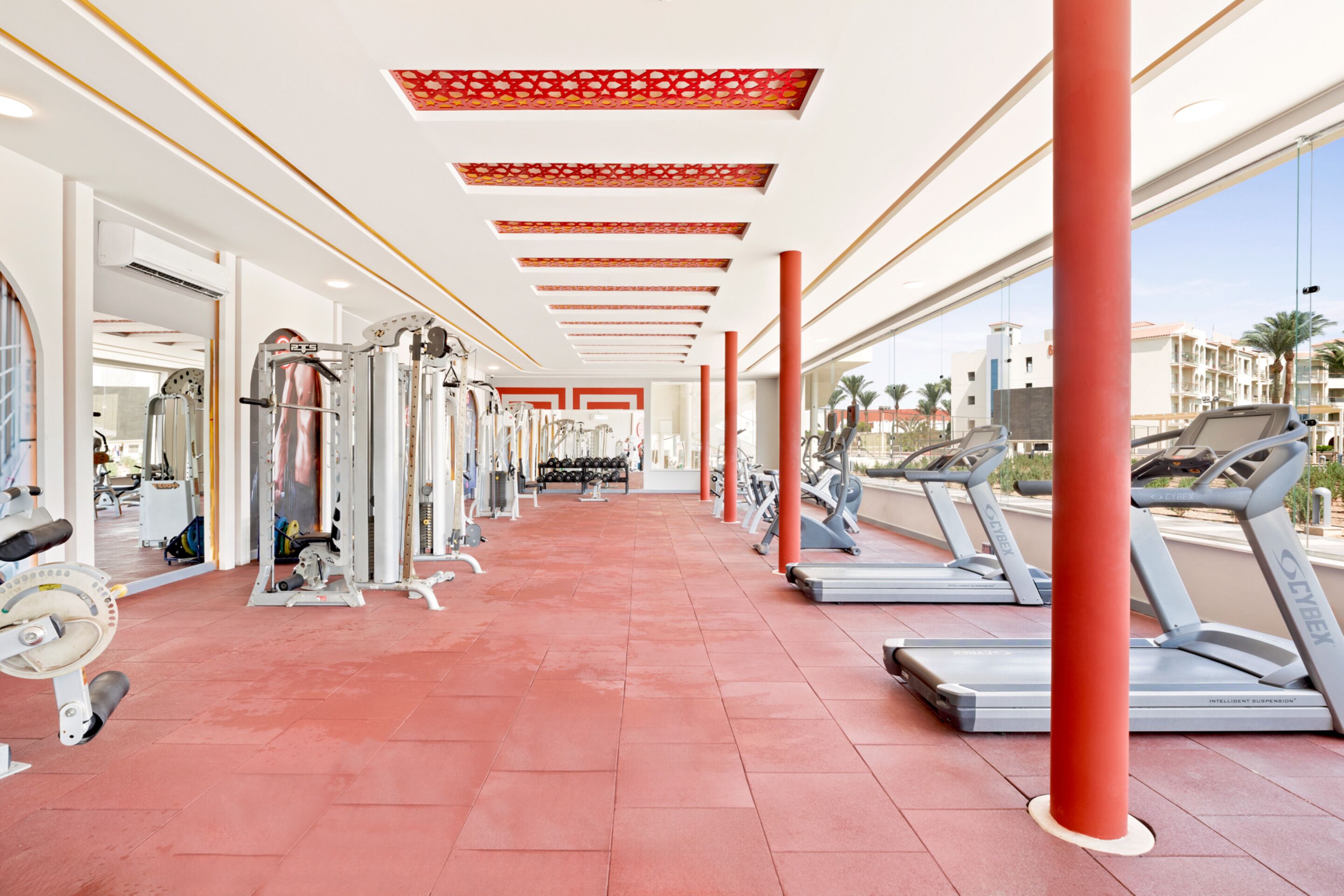 Une salle de sport équipée de tapis de course, d’appareils de musculation et dotée d’un sol recouvert de carreaux rouges.