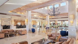 A spacious lobby with high ceilings, a grand chandelier, and a reception area with a counter and seating.