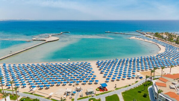 A beach resort with numerous blue umbrellas, a pier, and a clear view of the ocean.