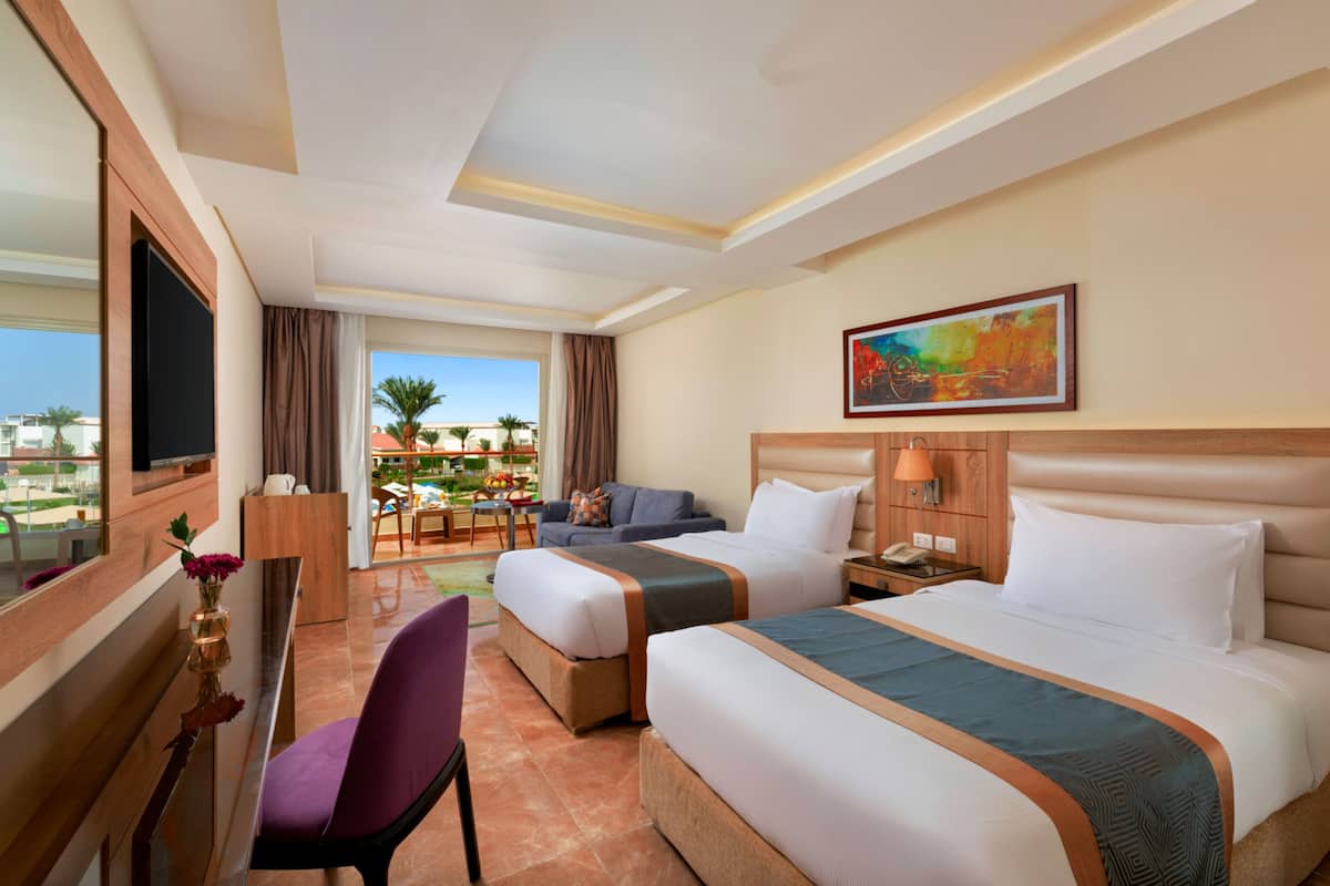 A hotel room with two beds, a desk with a TV, a chair, a painting on the wall, and a view of the outdoors.