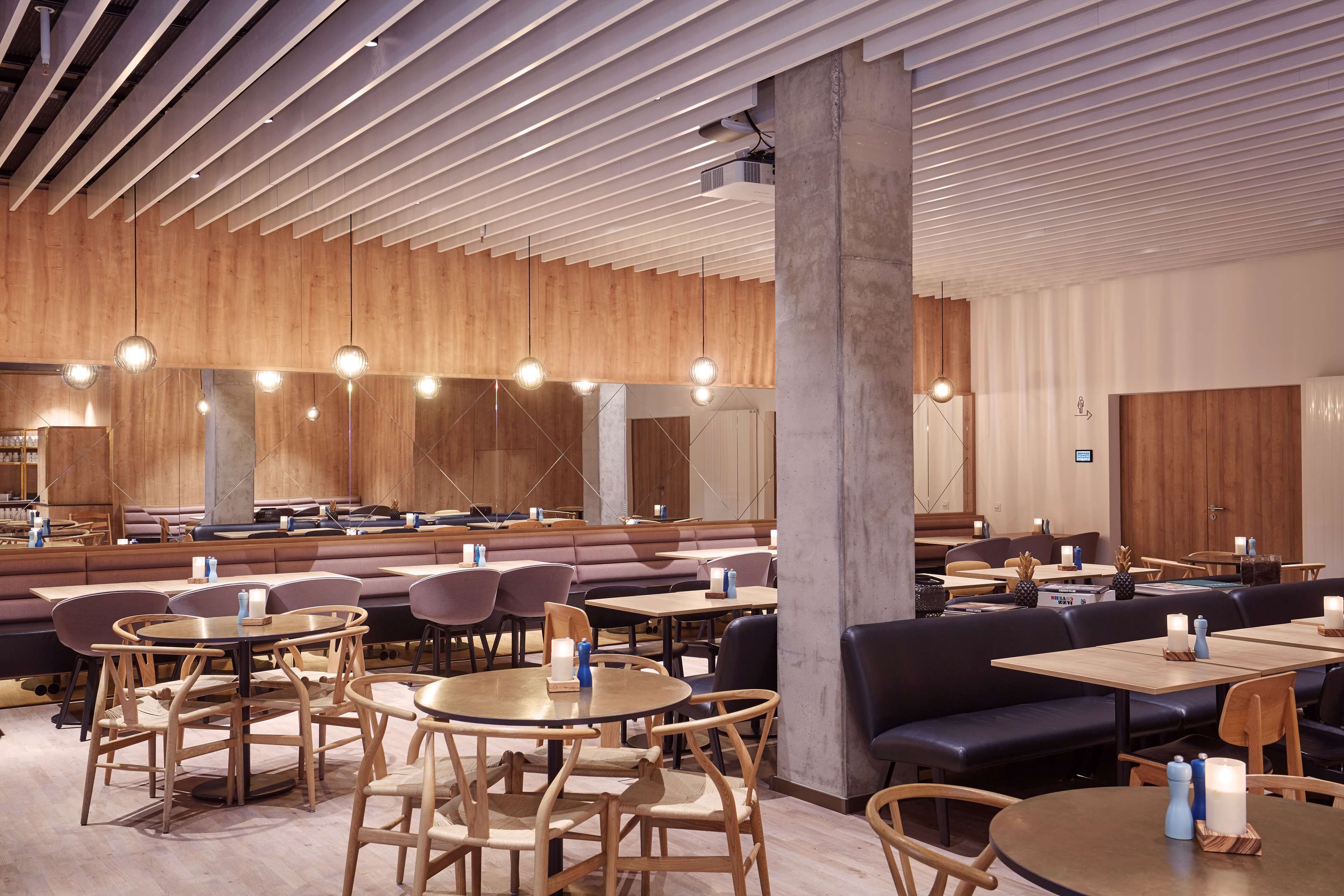 A modern restaurant with wooden panel walls, round tables, and black leather seating.