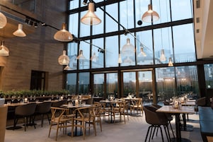 Un ristorante moderno con ampie finestre, tavoli in legno e lampade a sospensione.