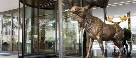 Une entrée moderne avec une porte en verre et une sculpture en bronze représentant un élan, placée devant le bâtiment.