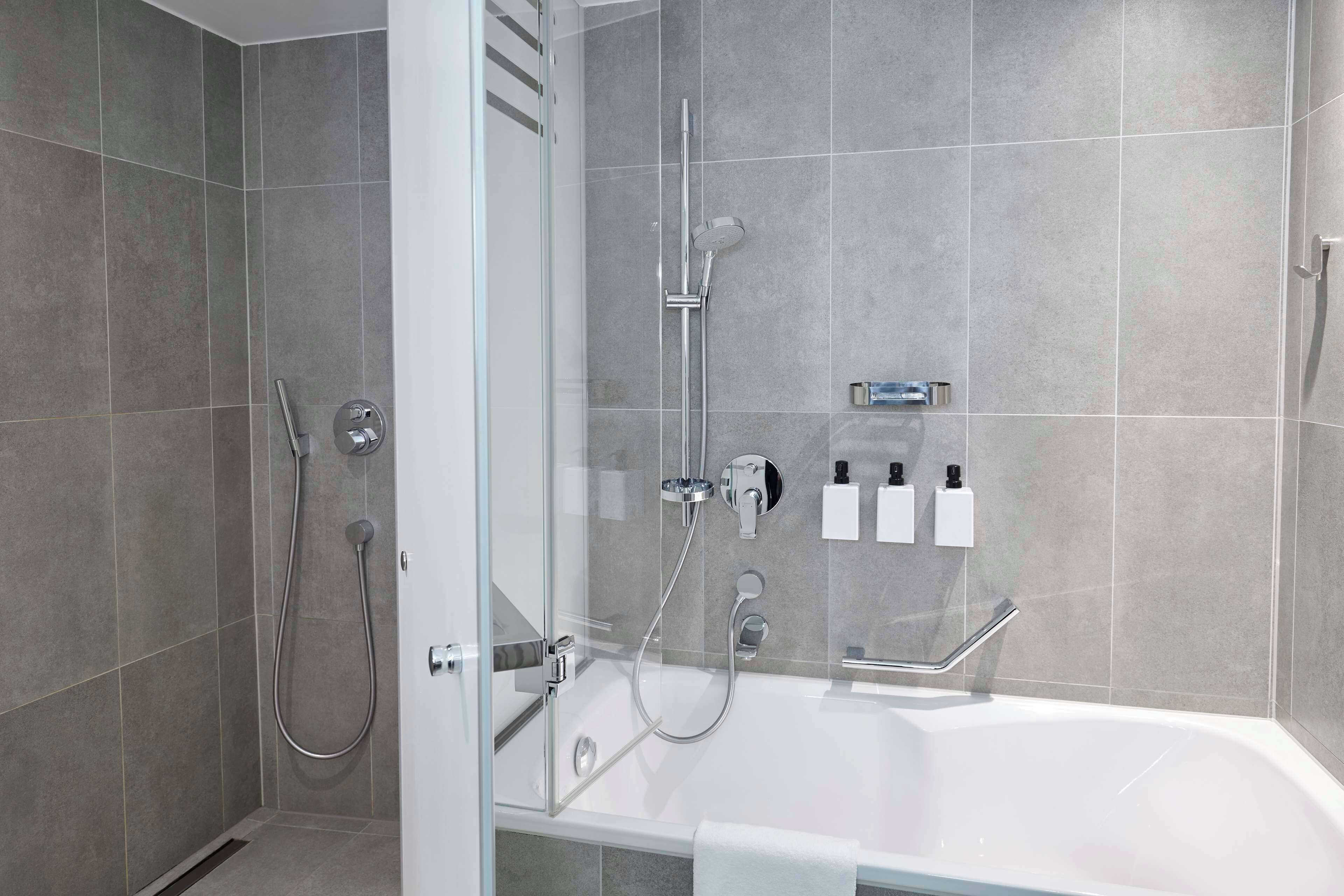 A modern bathroom with a glass-enclosed shower, a standalone bathtub, and a wall-mounted soap dispenser.