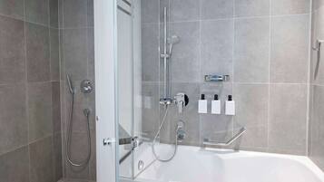 A modern bathroom with a glass-enclosed shower, a standalone bathtub, and a wall-mounted soap dispenser.