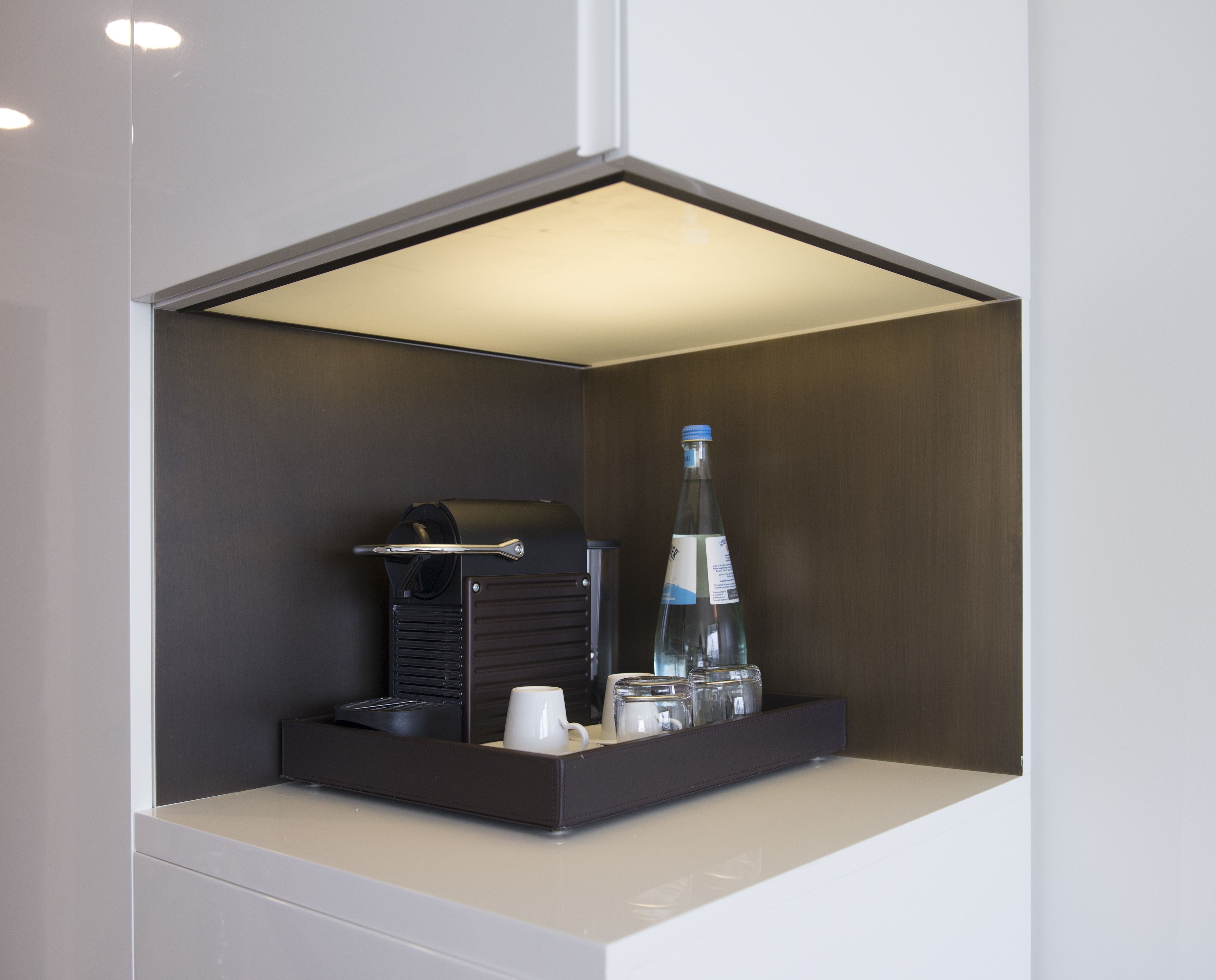 A compact minibar with a coffee maker, a bottle, and glassware.