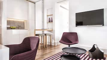 A modern living room with a flat-screen TV, two purple chairs, a small round table, and a dark brown bag on a striped rug.