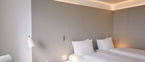 A modern hotel room with two beds, a bedside table, a floor lamp, and a small round table.