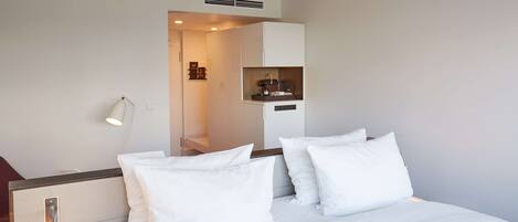 A hotel room with a neatly made bed, a bedside lamp, and a small kitchenette area.