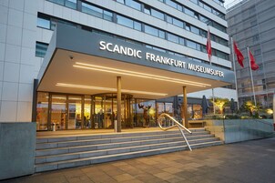 L'esterno dell'hotel Scandic Frankfurt Museumufer, caratterizzato da una facciata moderna, ampie finestre in vetro e una scalinata che conduce all'ingresso.