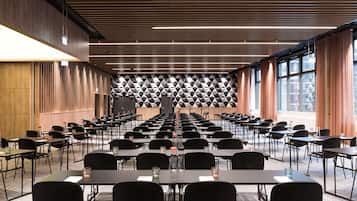 A conference room with rows of tables and chairs, a geometric patterned wall, and large windows with curtains.