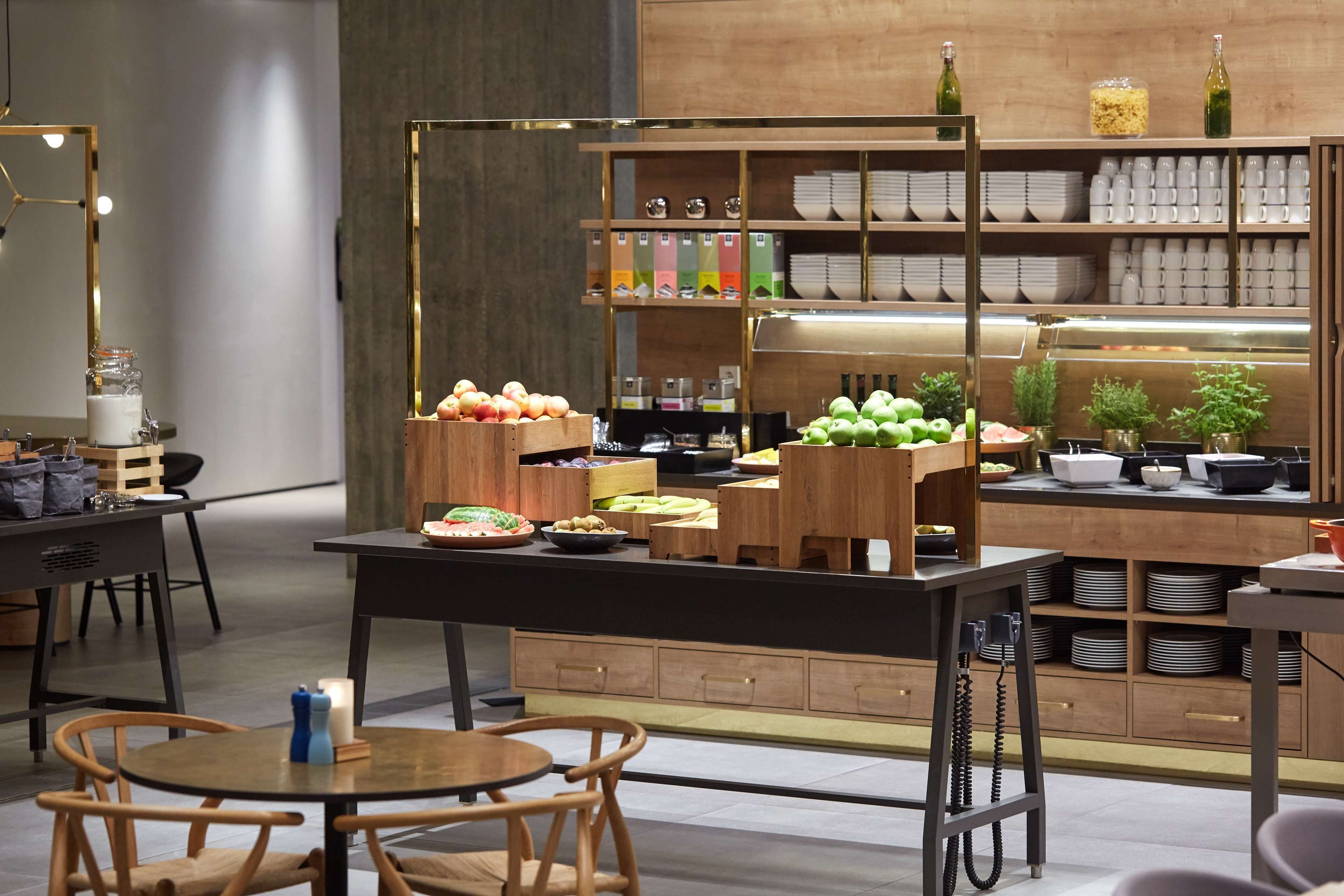 A modern kitchen with wooden cabinets, a central island with fruits and vegetables, and a variety of kitchenware on shelves.