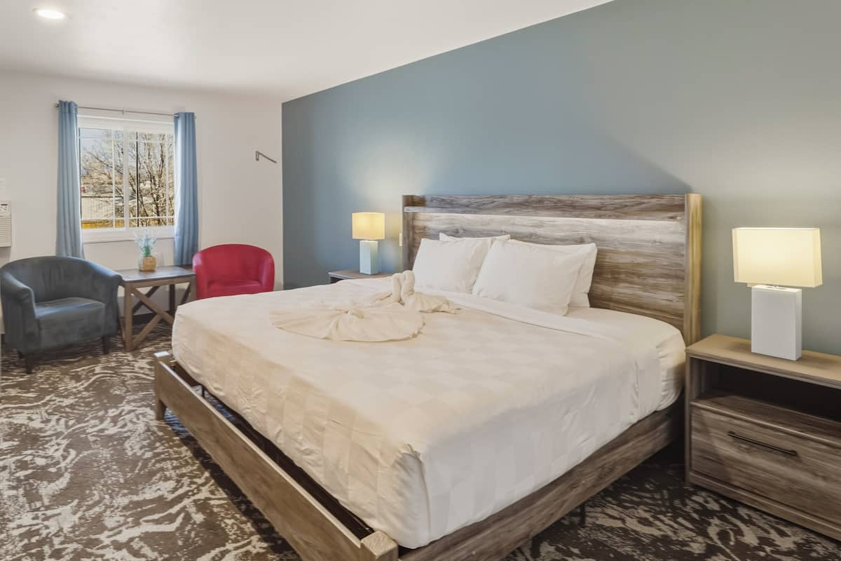 A hotel room with a large bed, two bedside tables, a desk, a chair, and a window with curtains.