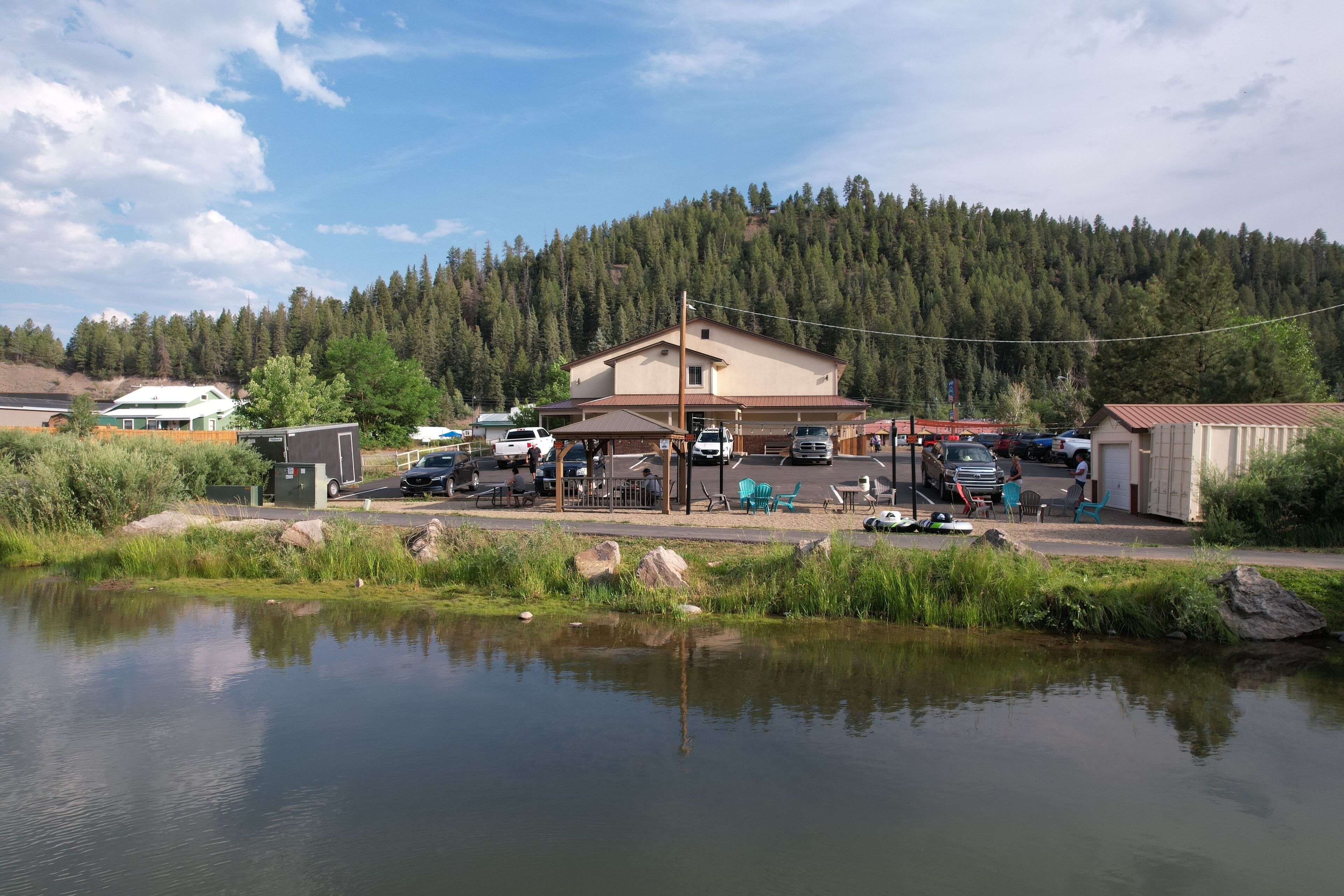 A lakeside building with a parking area and outdoor seating.