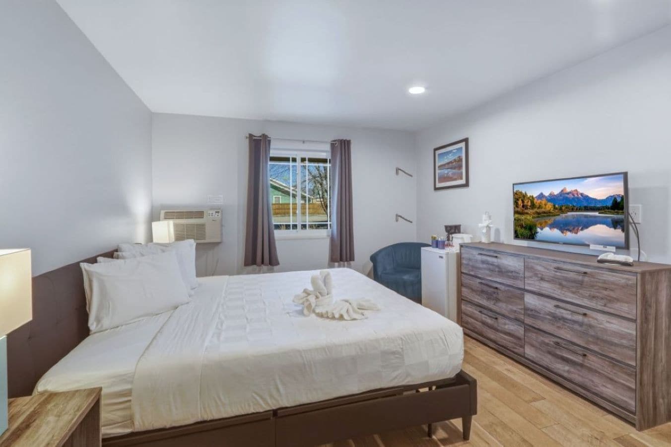 A hotel room with a bed, a desk, a television, and a window with curtains.