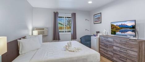 A hotel room with a bed, a desk, a television, and a window with curtains.