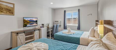 A hotel room with two beds, a desk, a TV, and a window with a view.