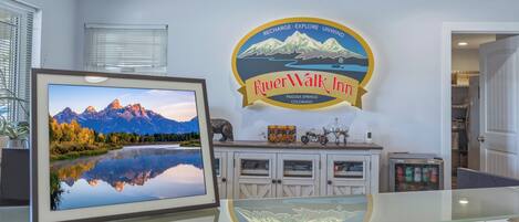 Zona de recepción de un hotel con una fotografía panorámica enmarcada, el logotipo de RiverWalk Inn y un mostrador con refrigerador.