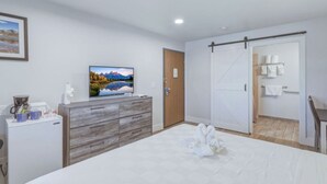 A bedroom with a bed, a TV, a dresser, a door, and a bathroom. - RiverWalk Inn (Pagosa Springs)