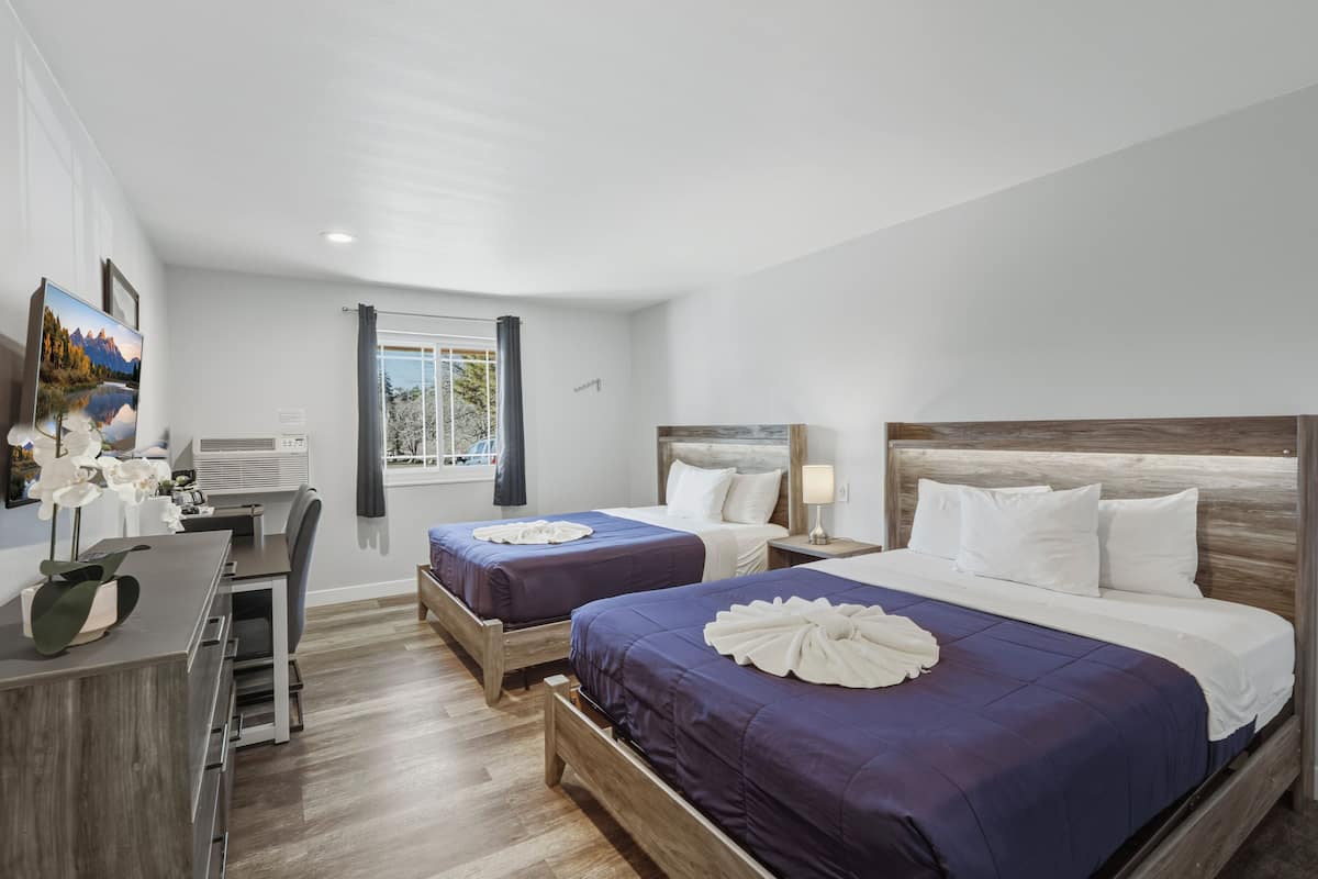 A hotel room with two beds, a desk, and a window with curtains.