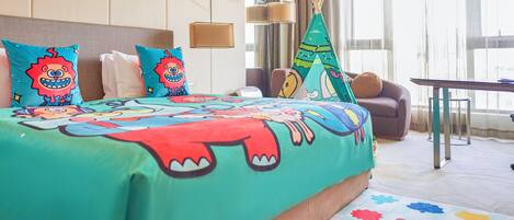 A hotel room with a bed, pillows, a sofa, a table, and a window with curtains.
