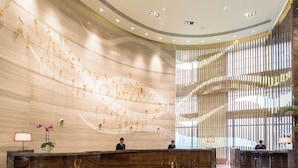 A modern lobby with a curved reception desk, a large wall mural, and a vertical wooden panel design. - Holiday Inn Shanghai Hongqiao by IHG (Shanghai)